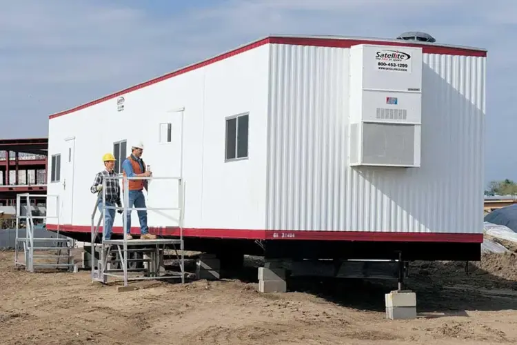 Two men entering a white mobile office trailer.