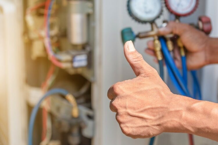 A person giving a thumbs-up while checking an HVAC unit.