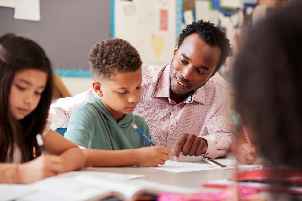 A teacher sitting next to a group of children, helping them with homework