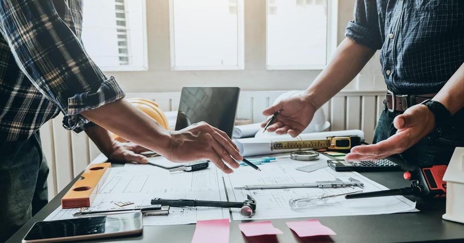 Two men standing over a work table discussing a modular construction design.