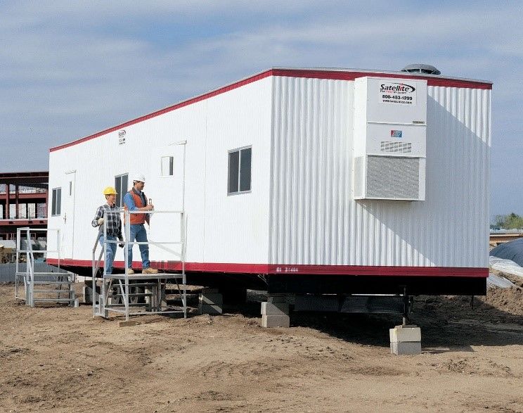 Two men about to enter a white mobile office on a job site.