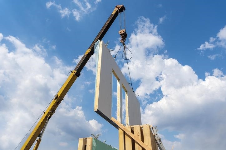 A crane lifting the wall of a modular building during construction.