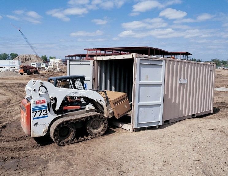 A small front loader placing a box into a storage container.