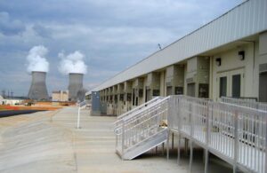 Exterior side view of a modular building with stairs leading to a ramp. In the background is a refinery silo. 