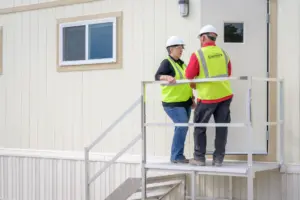 Satellite employees in high vis vests talk on the steps of a mobile office 3