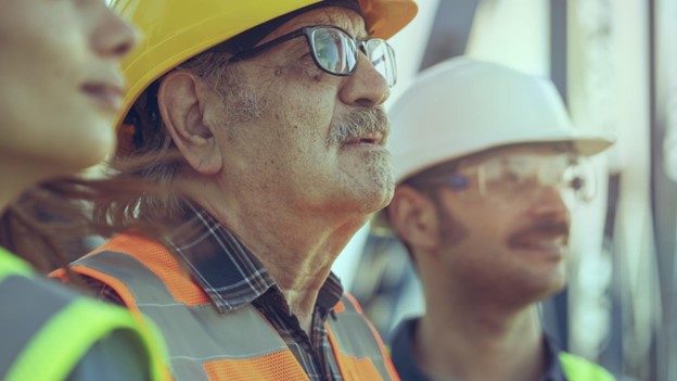 a group of people wearing construction hats and vests looking off in the distance