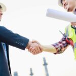 A construction worker and a businessman shake hands