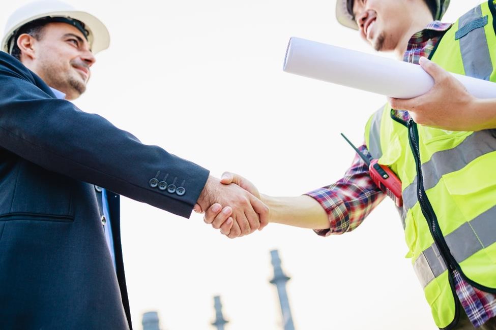 A construction worker and a businessman shake hands