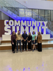 Employees standing in front of community summit sign