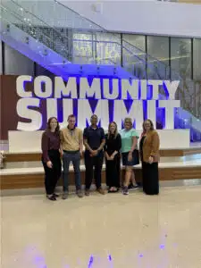 Employees standing in front of community summit sign.