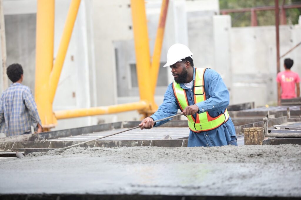 A construction worker in a safety vest and helmet smooths wet concrete at a construction site.