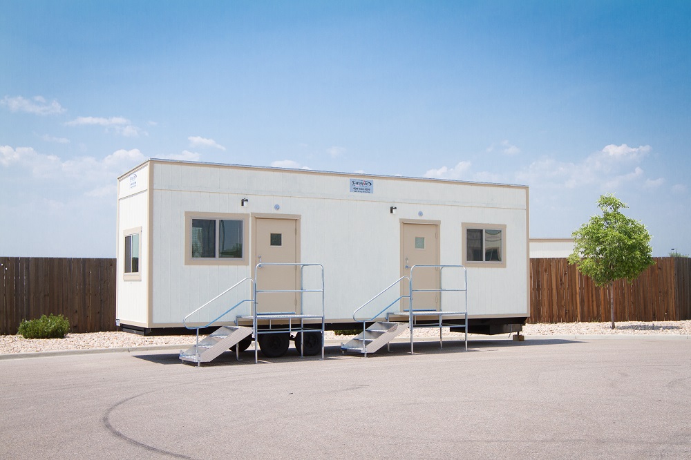 White mobile office with 2 exterior doors and steps leading up to the doors.