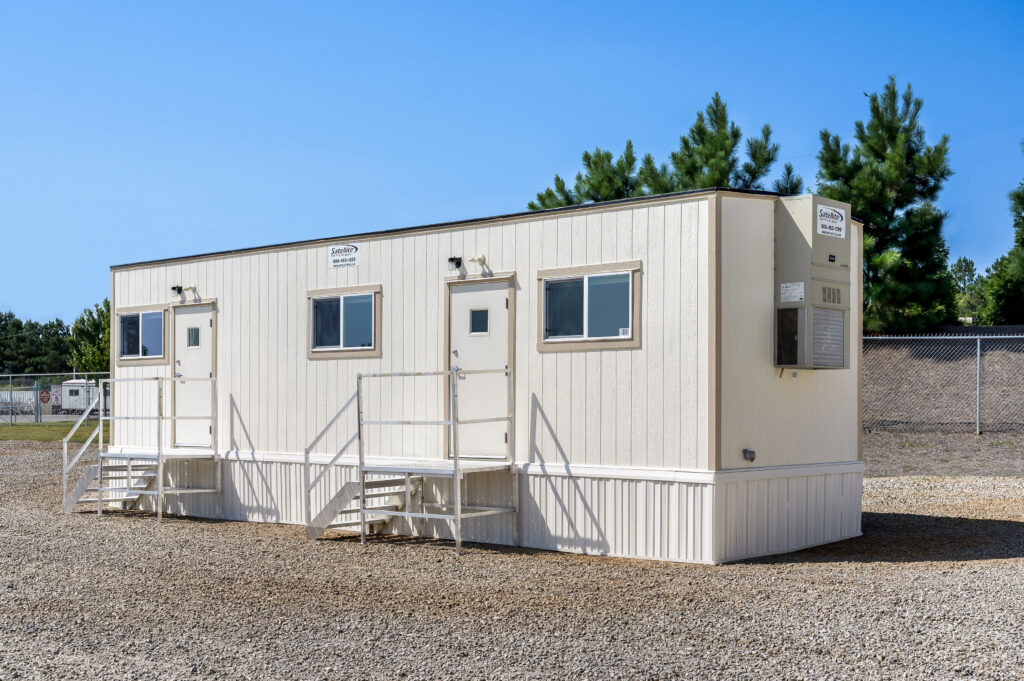 Side view of a 10x40 mobile office with an HVAC unit and skirting around building. Mobile office has 2 exterior doors with steps leading up.