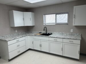 Interior kitchen in a custom modular office. Featuring white upper and lower cabinets, grey countertops and sink