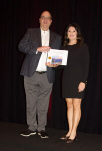 Two team members standing on a stage holding a certificate 