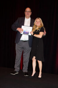 Two team members standing on a stage holding a certificate. 