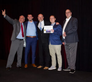 5 team members standing on a stage with a certificate 