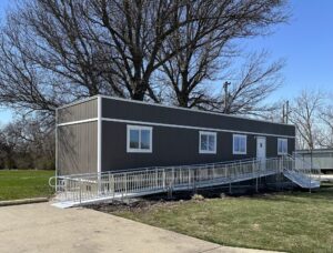 A construction office trailer on a job site with a ramp and stairs coming off a single door.