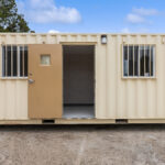 External view of a ground-level office with the door open to view inside the storage container, 2 windows with security bars on the windows.