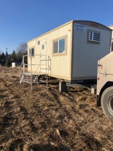 A mobile office trailer hitched to a vehicle in a dirt field.