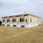 4-plex modular building with white skirting around the base of the mobile offices. HVAC units located on the end of each unit and a windfarm wind turbine located behind the office.