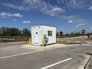 8x12 guard shack with an external door sitting at the entrance of a road with 2 barriers