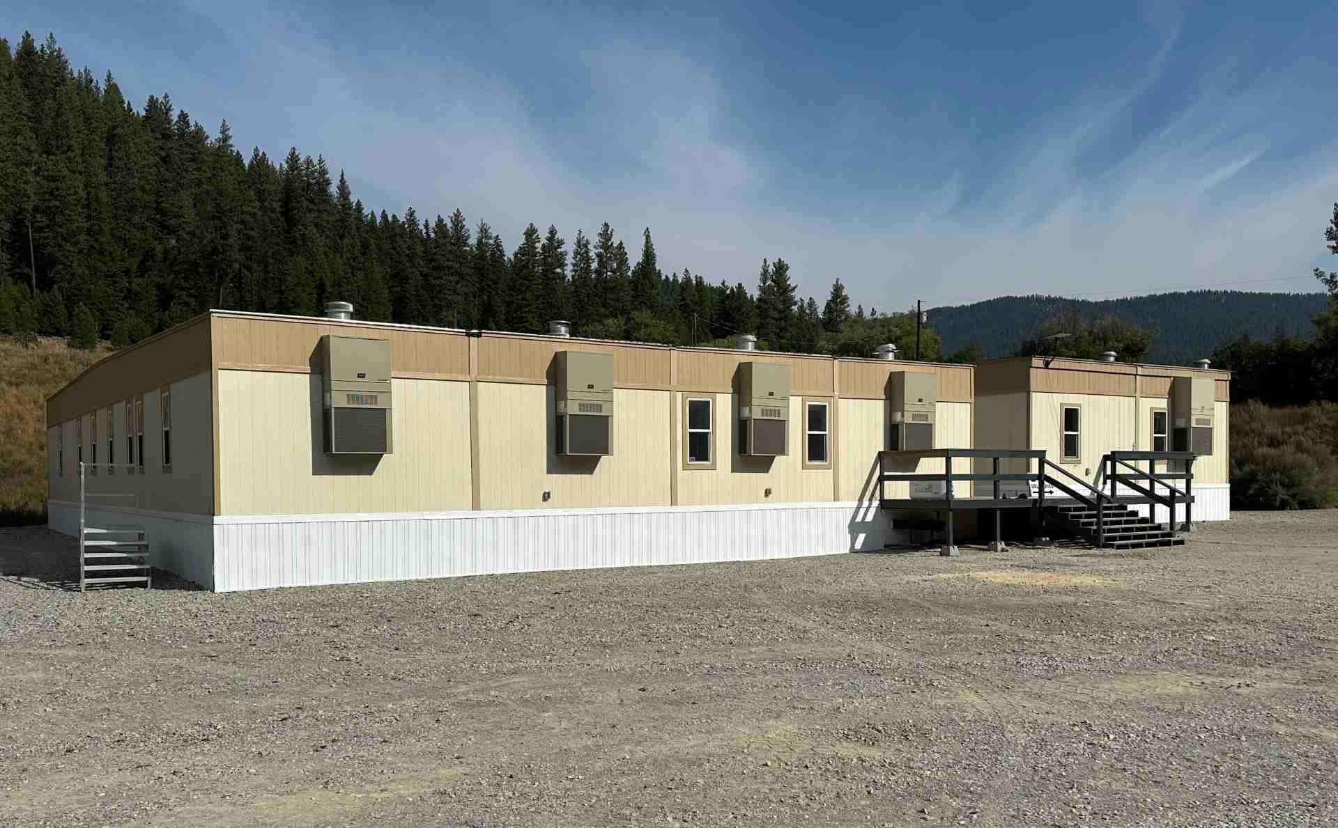An excavator working beside portable office trailers on a construction site with trees.