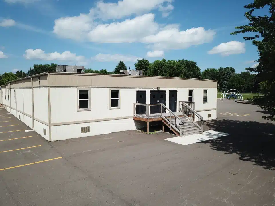 Portable classrooms on a blacktop lot by a playground at a school.