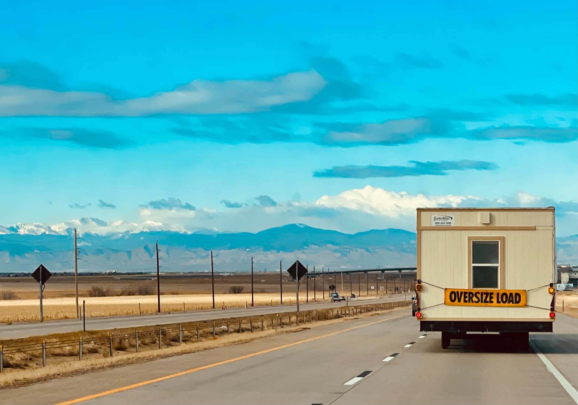 A truck hauling a mobile office with an "overside load" sign on the back of it.