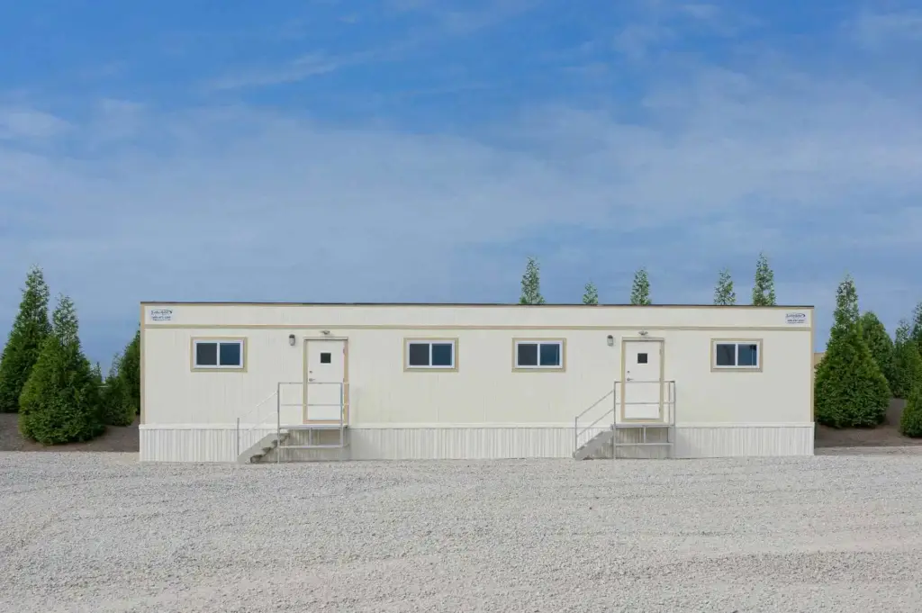 A doublewide mobile office trailer sitting on a gravel lot.