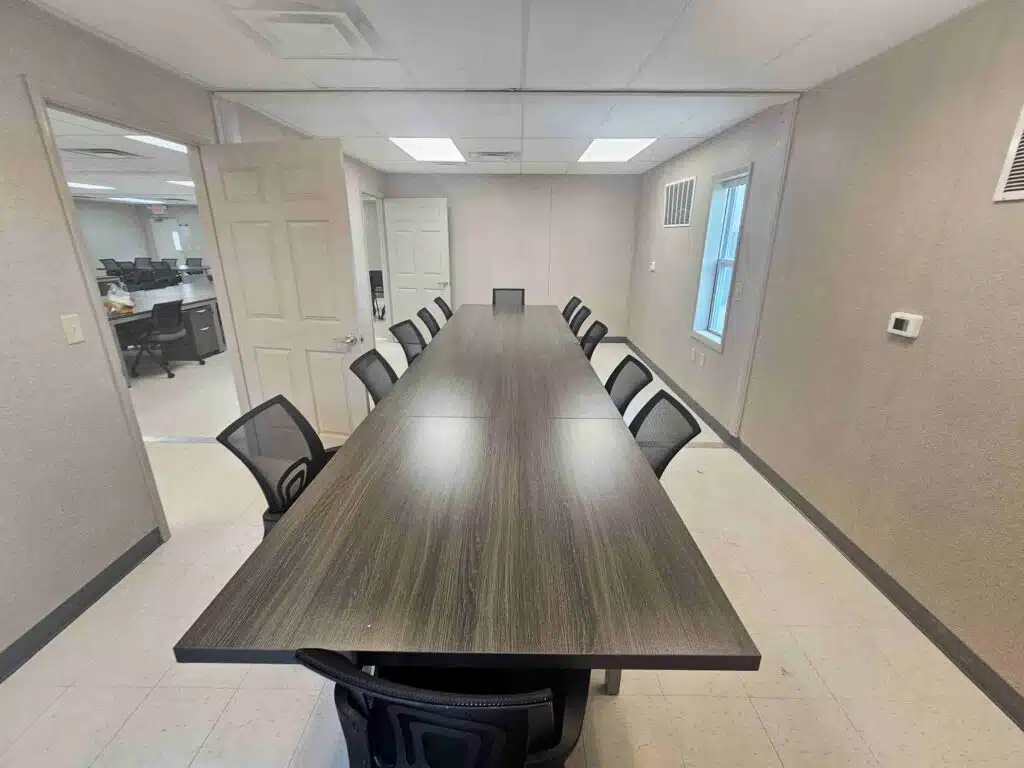 Indoor, empty training room with long conference table and black office chairs surrounding the table.